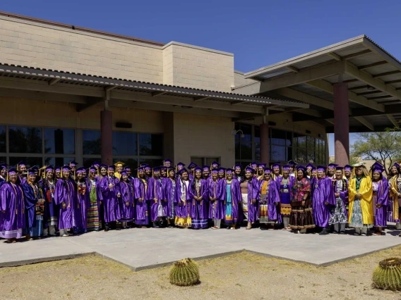 a group of graduates, mostly in purple caps and gowns, posing for a group photo at Tohono O'odham Community College