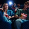 A young man feeling bored while watching film projection with his girlfriend in movie theater.