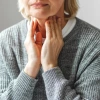 a closeup of the torso on an older adult who is lightly touching their own neck with both hands